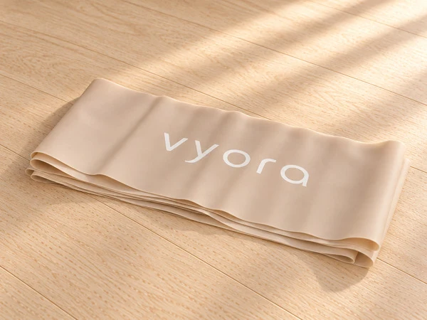Das lange vyora Gymnastikband in Beige, ordentlich gefaltet, mit weißem vyora-Schriftzug auf einem hellen Holzboden im Sonnenlicht