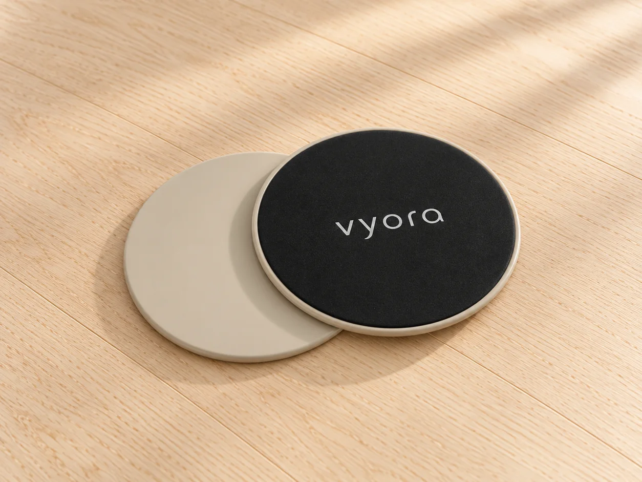 Zwei vyora Slider auf einem Holzboden, einer mit der glatten hellen Seite, einer mit der schwarzen textilen Seite nach oben