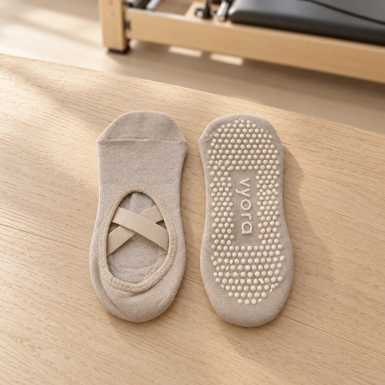 Ein Paar vyora Anti-Slip-Socken auf einem Holzboden: eine von oben mit überkreuzten Riemen, eine mit der Noppensohle und dem vyora-Schriftzug